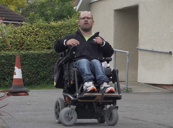 Our wheelchair skills trainer in his powered chair outside a single story building