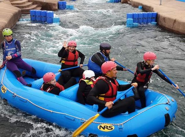 A group of young wheelchair users are in a blue raft going down some white water rafts