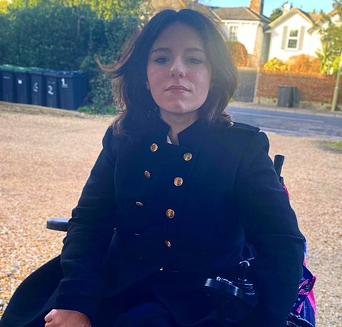 Faith Martin portrait photo, outside. She is wearing a black coat with brass coloured buttons.