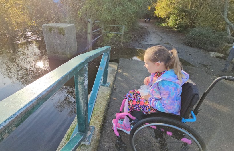 A young wheelchair user sits by the side of a lake
