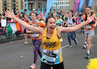 An incredible Whizz Kidz runner has her arms open as she runs past a Whizz Kidz cheer point