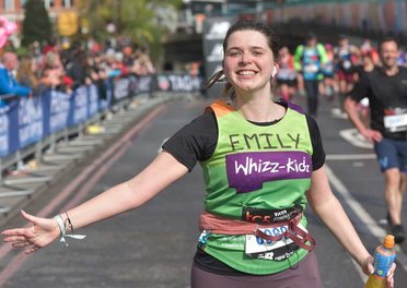 A runner in a green Whizz Kidz top runs with her arm out smiling