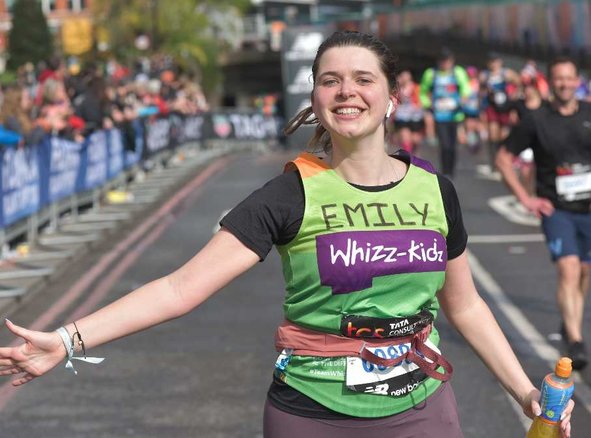 A runner in a green Whizz Kidz top runs with her arm out smiling