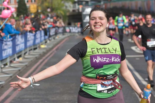 A runner in a green Whizz Kidz top runs with her arm out smiling