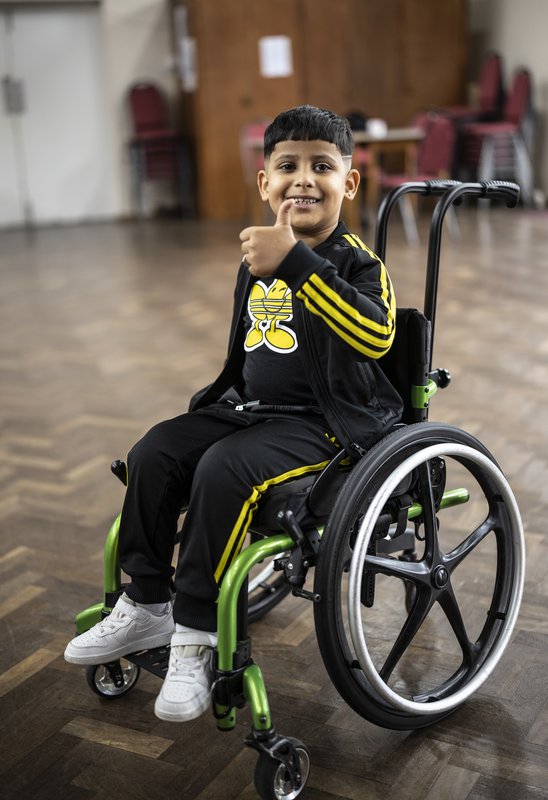 Isaac sits in his wheelchair, which has green detailing, with his thumb up. He's smiling.