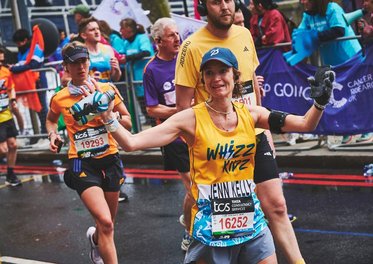 A runner in a yellow Whizz Kidz vest waves to a Whizz Kidz cheer point