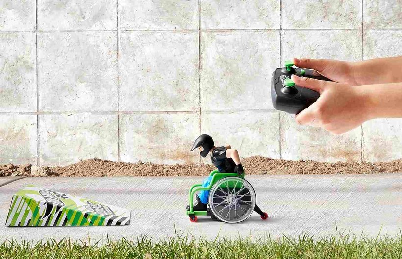Scene showing a Hot Wheels remote control wheelchair user and some hands with the remote control. He is about to take off from a ramp.