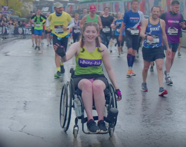 Ella waves to the camera as she completes the London Marathon in her manual wheelchair