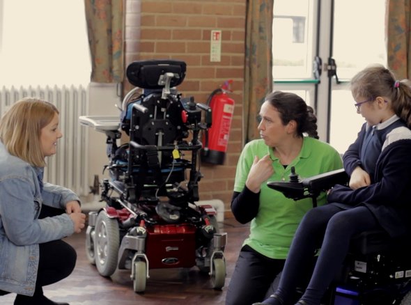 A Whizz Kidz clinician speaks with a young wheelchair user and her mother