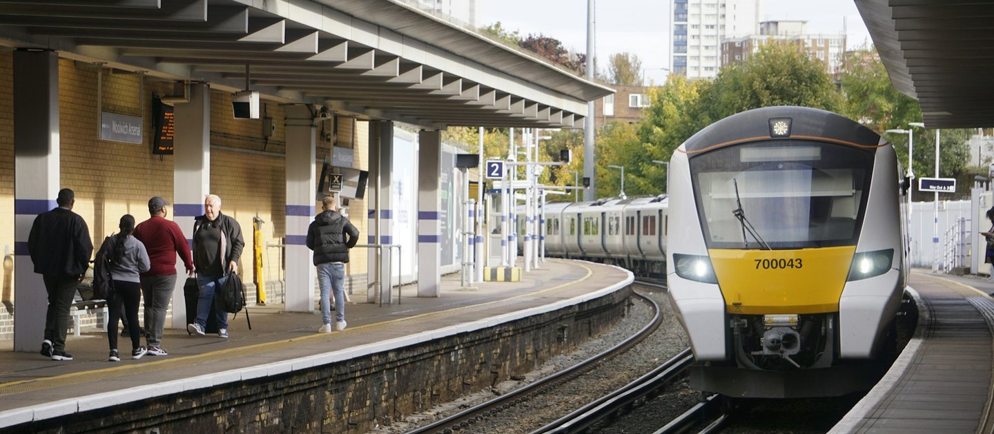 A train pulls up at a station with people standing on the platform opposite