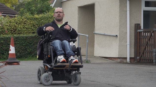 Our wheelchair skills trainer in his powered chair outside a single story building