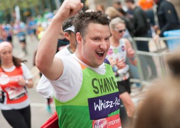 A runner in a green Whizz Kidz top raised his arm as he runs past the camera