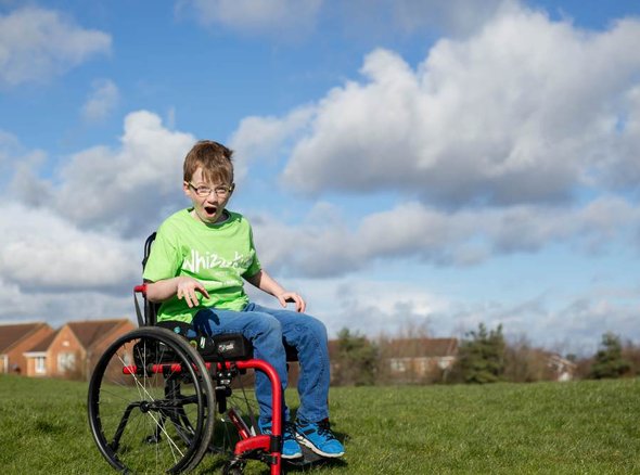 McKenzie wears a green Whizz-Kidz T-shirt in a manual wheelchair in an open field