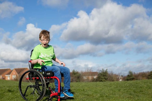 McKenzie wears a green Whizz-Kidz T-shirt in a manual wheelchair in an open field