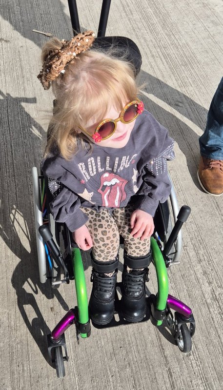 Charlie sits in her green and purple wheelchair, wearing some trademark supercool shades.