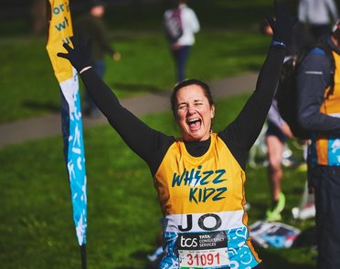 A runner in a yellow Whizz Kidz running vest hold her hands in the air