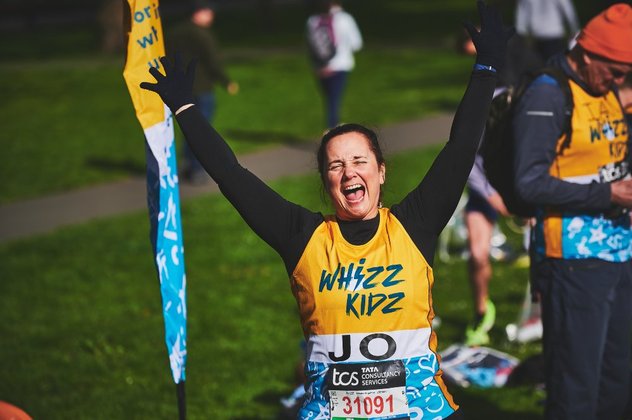 A runner in a yellow Whizz Kidz running vest hold her hands in the air