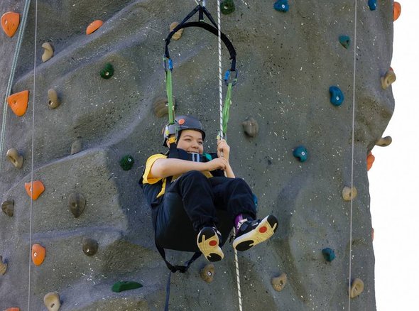 A young wheelchair user is hoisted down after climbing up an outdoor climbing wall