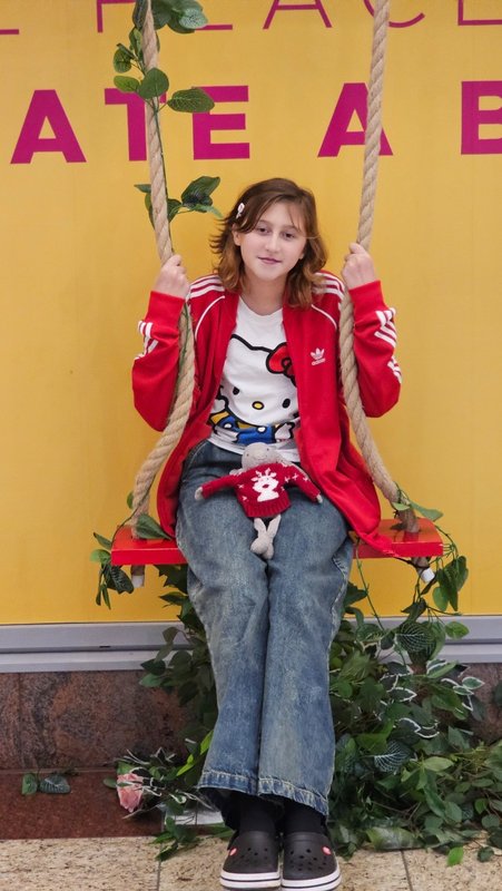 Ivy sits on a swing wearing a Helly Kitty t-shirt, jeans and a red Adidas zip top.
