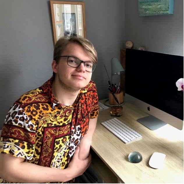 A young adult sits at a neat desk with a computer in front of him