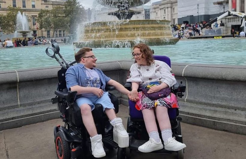 Two wheelchair-users holding hands in front of a large fountain