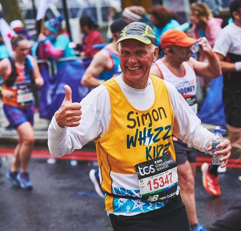 A runner in a yellow Whizz Kidz running vest gives us a thumbs up
