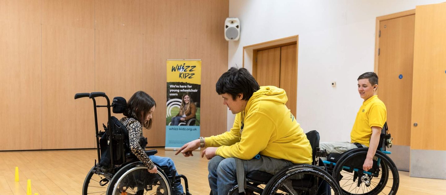 Rich and Nix, our wheelchair skills trainers help a young wheelchair user during one of their skills courses inside a sports hall
