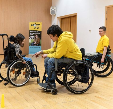 Rich and Nix, our wheelchair skills trainers help a young wheelchair user during one of their skills courses inside a sports hall
