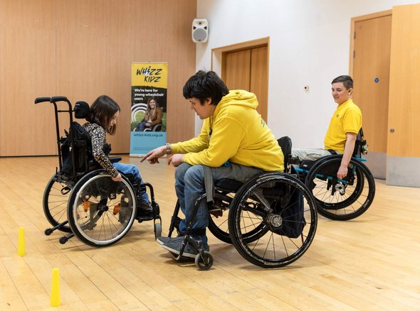 Rich and Nix, our wheelchair skills trainers help a young wheelchair user during one of their skills courses inside a sports hall