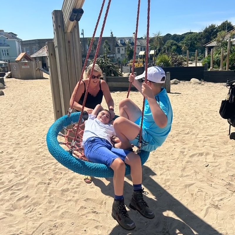 Tyler, his Mum and his brother playing on a swing together