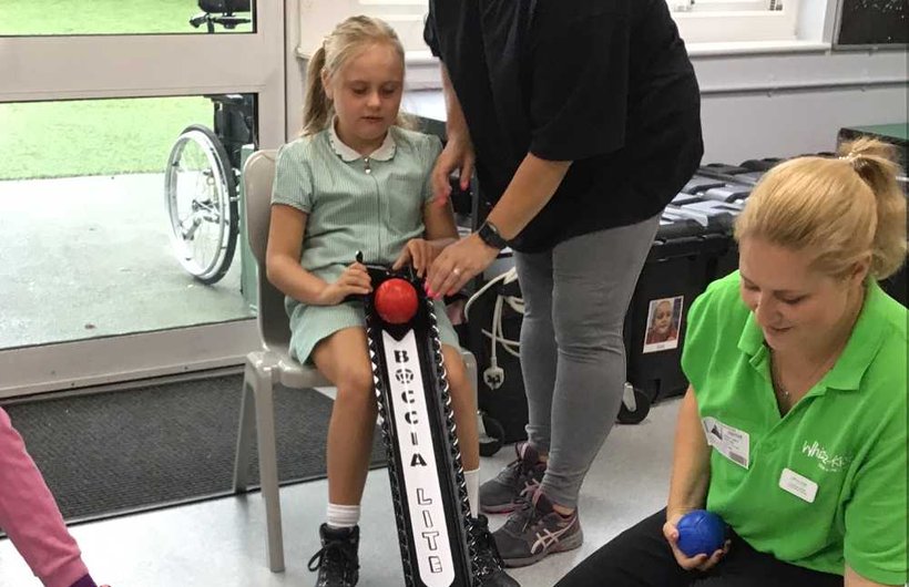 A young wheelchair user plays boccia with a Whizz Kidz team member sat next to her on the floor