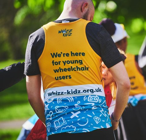 The back of our incredibly stylish yellow running vest. It reads "we're here for young wheelchair users"