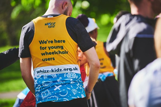 The back of our incredibly stylish yellow running vest. It reads "we're here for young wheelchair users"