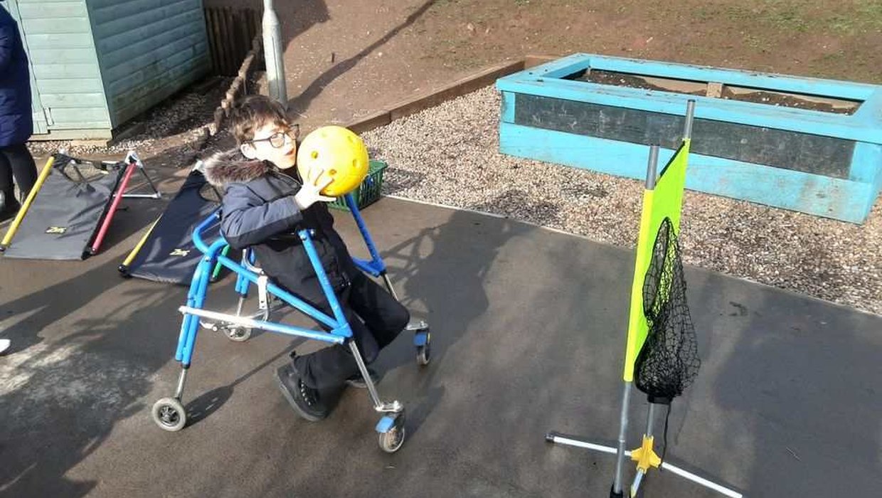 A young wheelchair user throws a ball into a net