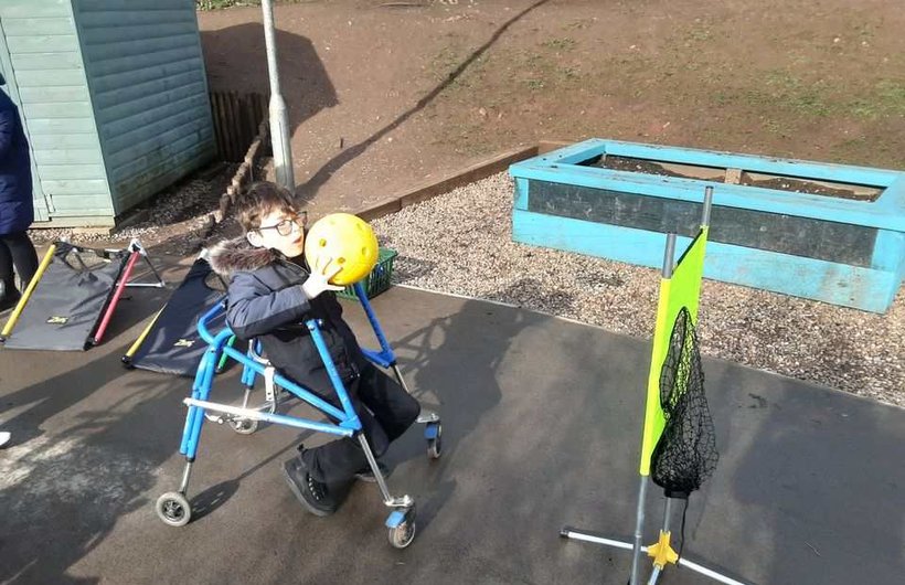 A young wheelchair user throws a ball into a net