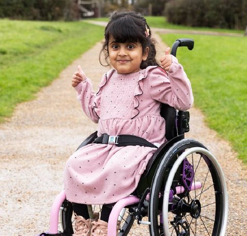 Aniyah outside in her new wheelchair from Whizz KIdz. She is giving a thumbs up and smiling at the camera.