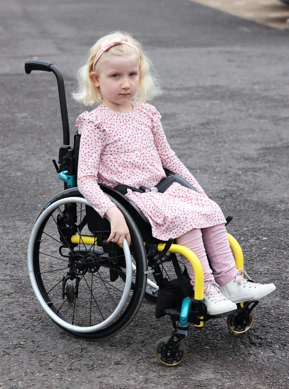 Nina, a blonde girl in a dress, sits in her wheelchair outside.