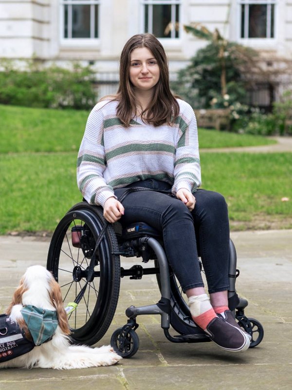 Ella from Kidz Board portrait. She is outside, smiling at the camera. There is grass and a building behind her.