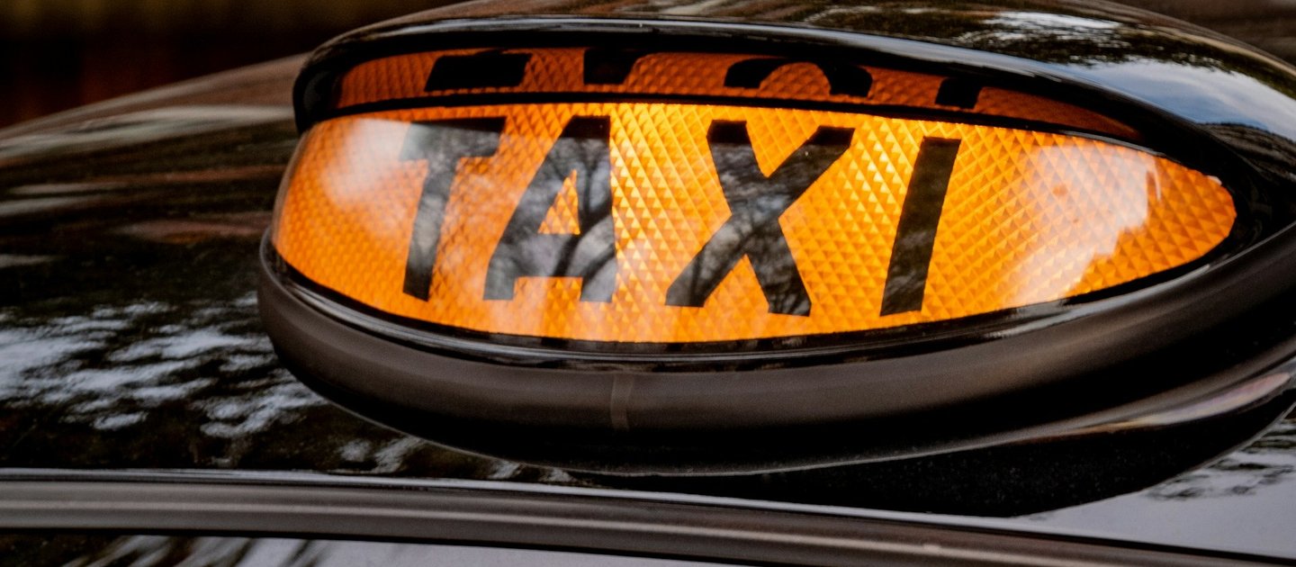 A close up of a taxi sign on-top of a black cab