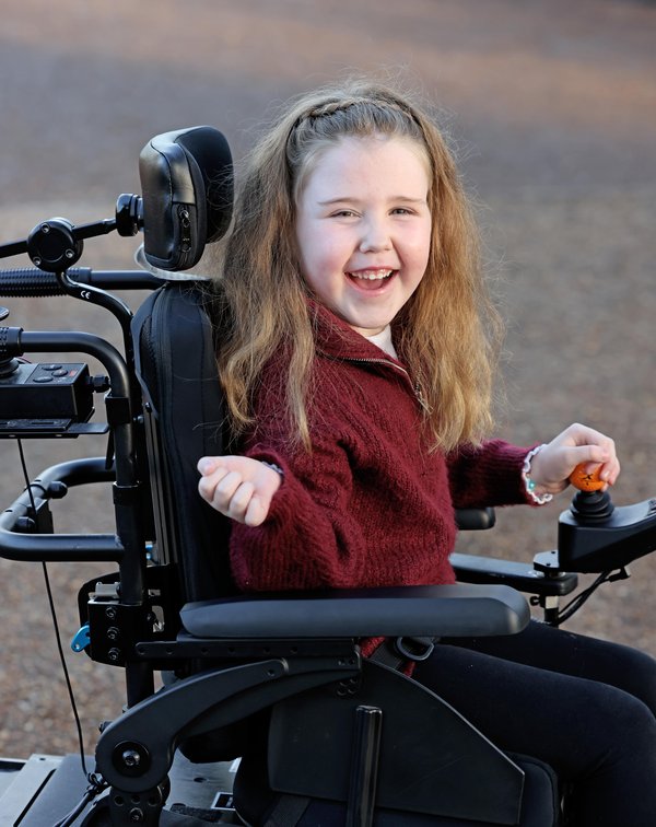 A close up photo of Margot, who is smiling and operating her powered wheelchair using the joystick