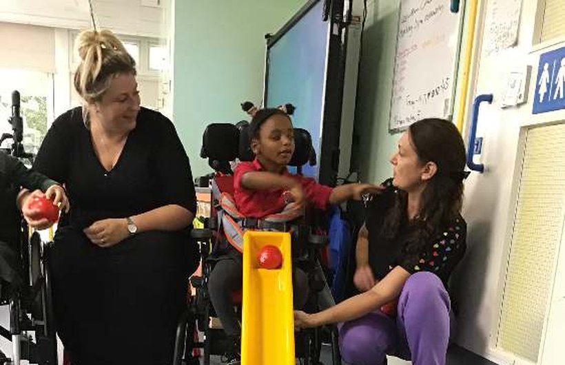 A young wheelchair user plays boccia with two adults either side of her