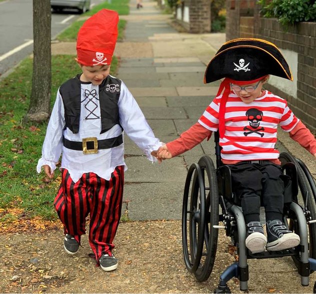 A young wheelchair user and their sibling go along a pavement hand in hand