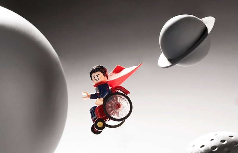 Wheelchair Superman mini-figure photographed flying through a space setting in his chair.