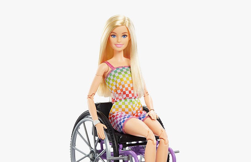 Barbie in her wheelchair wearing a rainbow checkerboard shorts and top.
