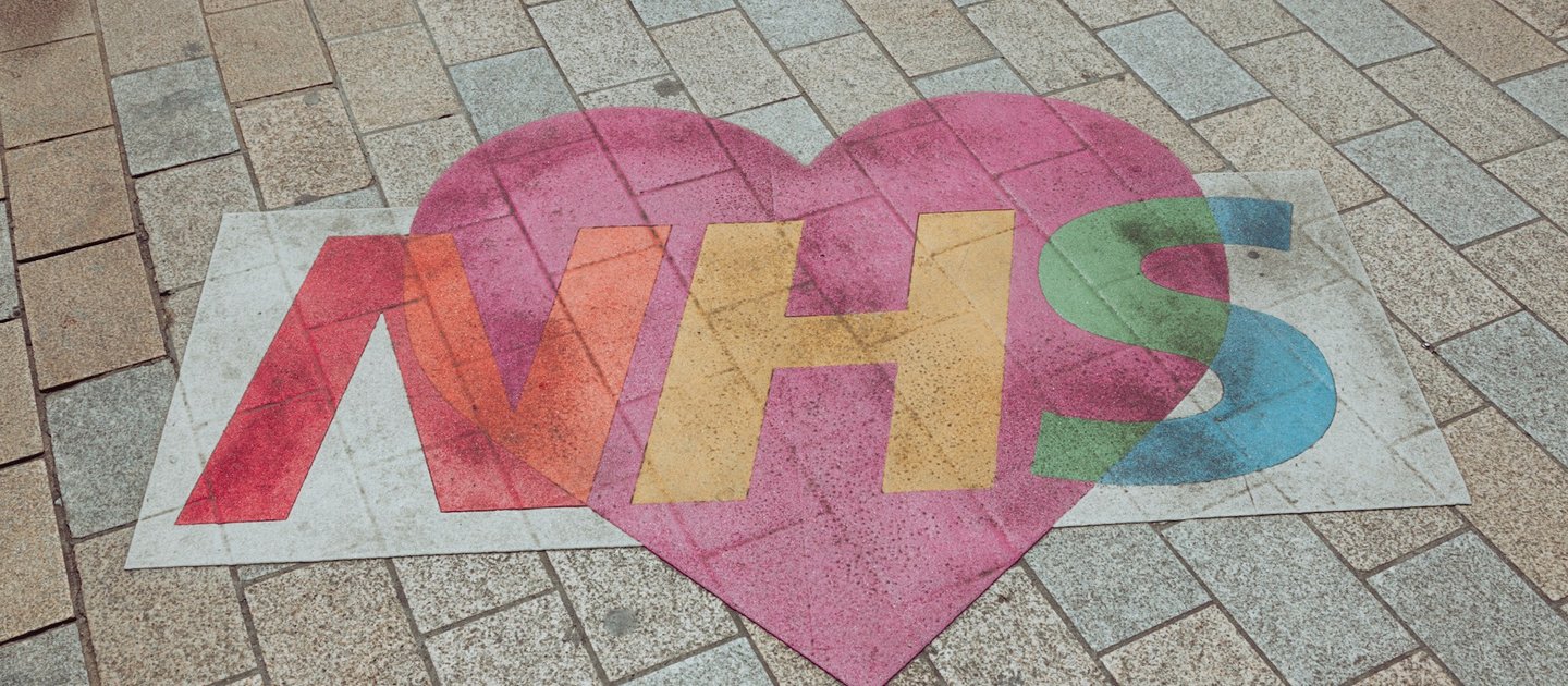 A colourful version of the NHS logo is drawn on a pavement over a heart