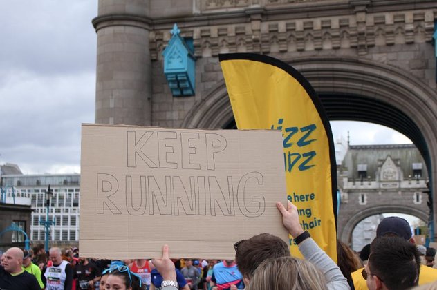 A carboard sign that reads 'keep running' is held up in front of a Whizz Kidz flag