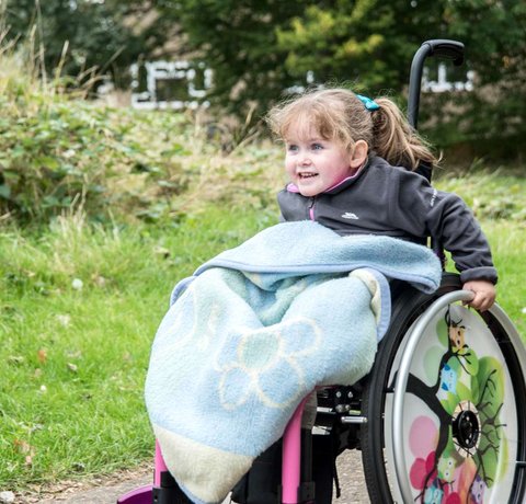 A young wheelchair user smiles as she pushes herself forward in a park