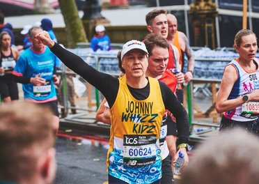 A runner in a yellow Whizz Kidz vest waves to a Whizz Kidz cheer point