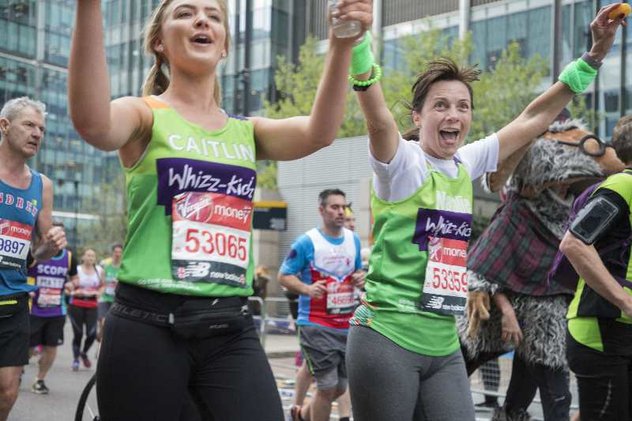 Two Whizz Kidz marathon runners, hold their hands up whilst looking incredibly stylish in their Whizz Kidz vests