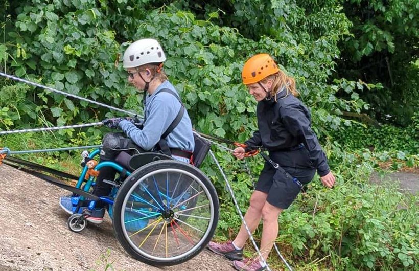 Rebecca abseiling in her wheelchair down a steep incline. An instructor is behind her.